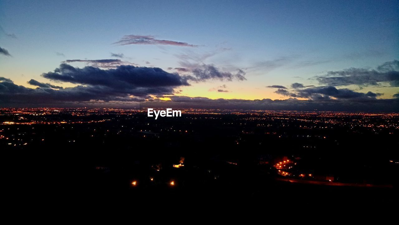 AERIAL VIEW OF ILLUMINATED CITYSCAPE AGAINST SKY AT SUNSET