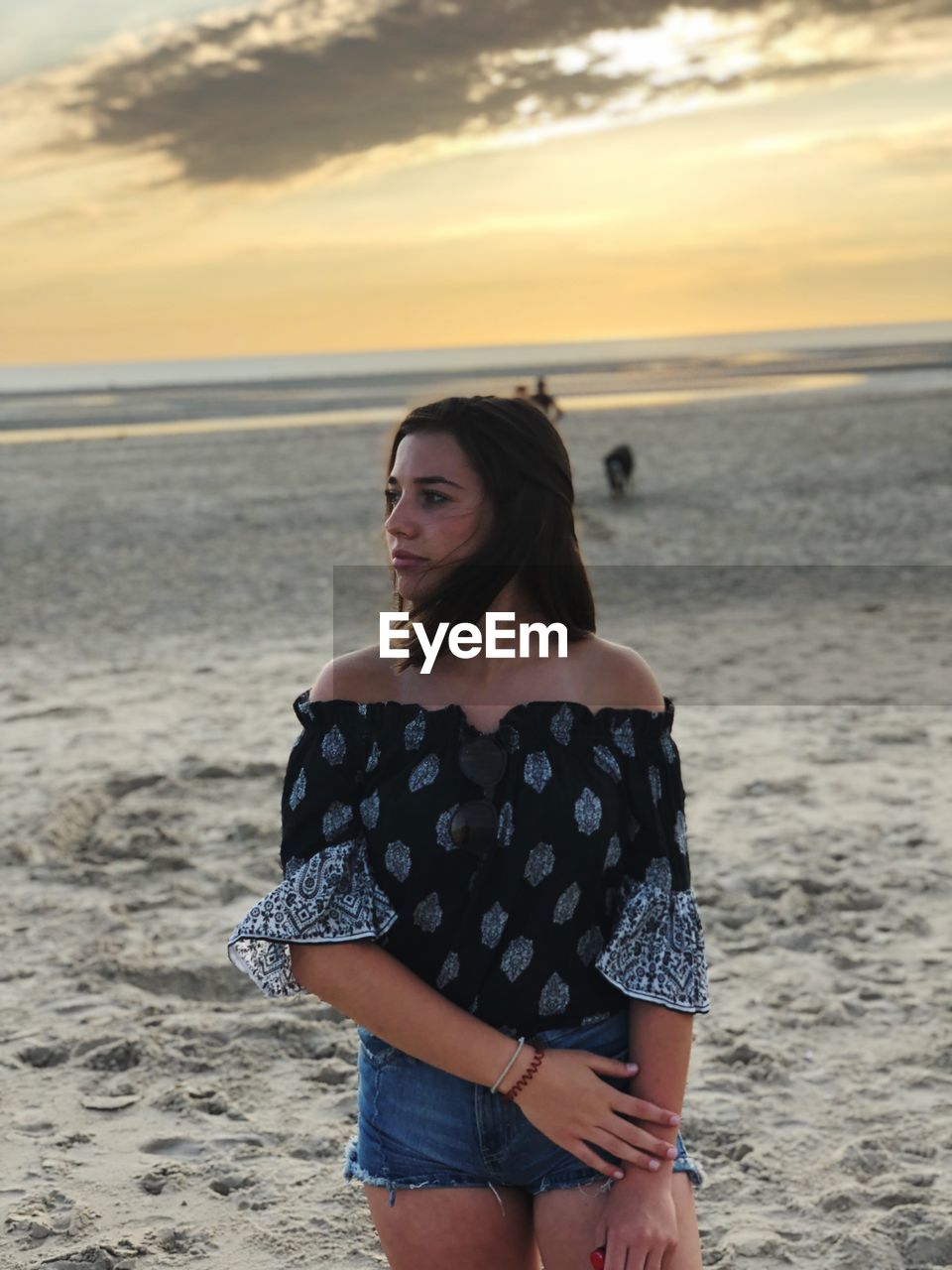 Thoughtful teenage girl standing at beach during sunset