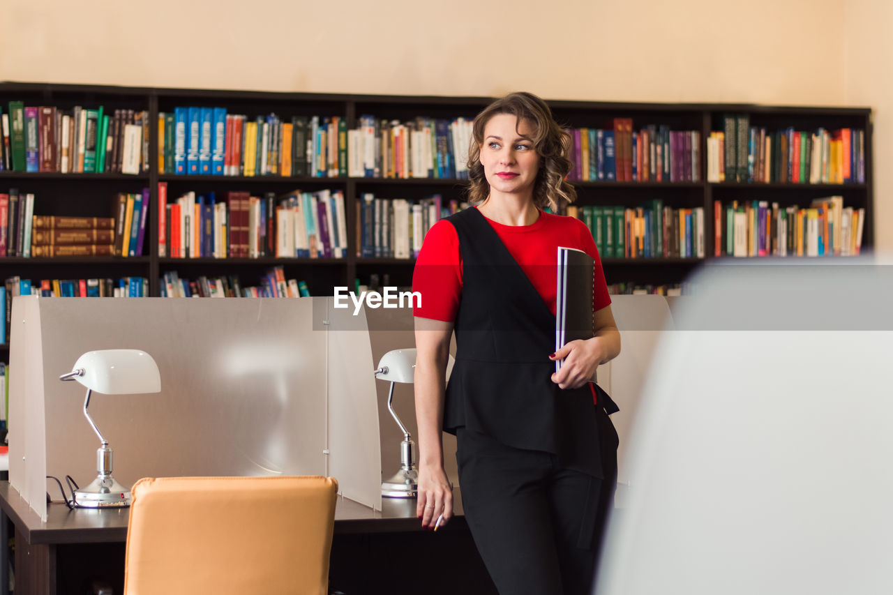 Professional woman educator or manager posing at public library of high school or college