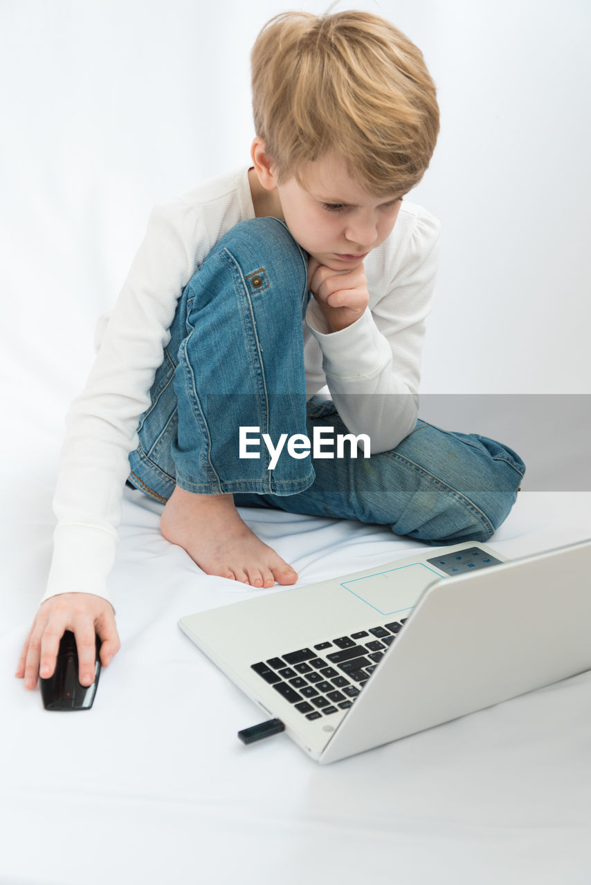 REAR VIEW OF BOY USING MOBILE PHONE IN LAPTOP