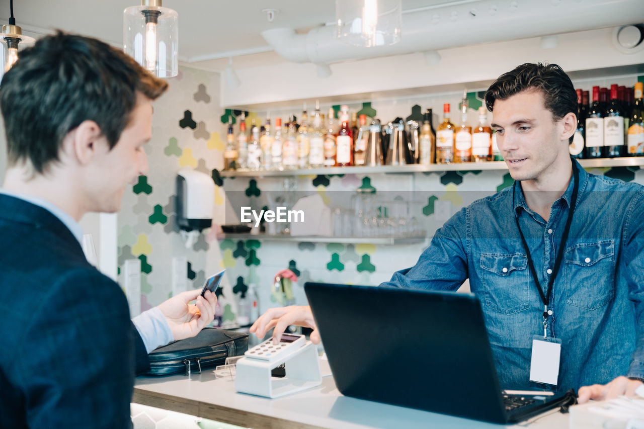 Businessman paying to owner with credit card at cash counter in cafe