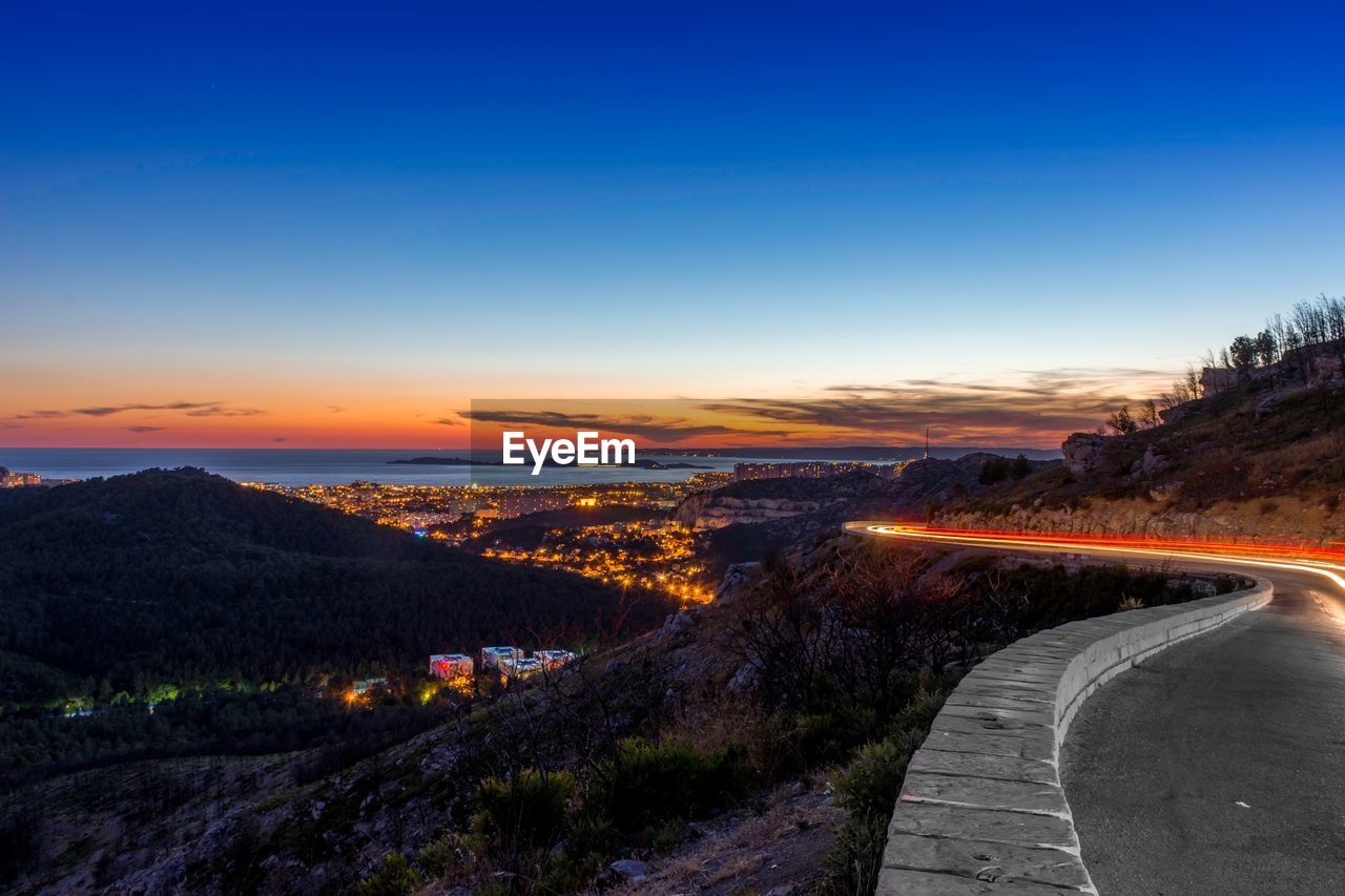 Illuminated road against sky during sunset