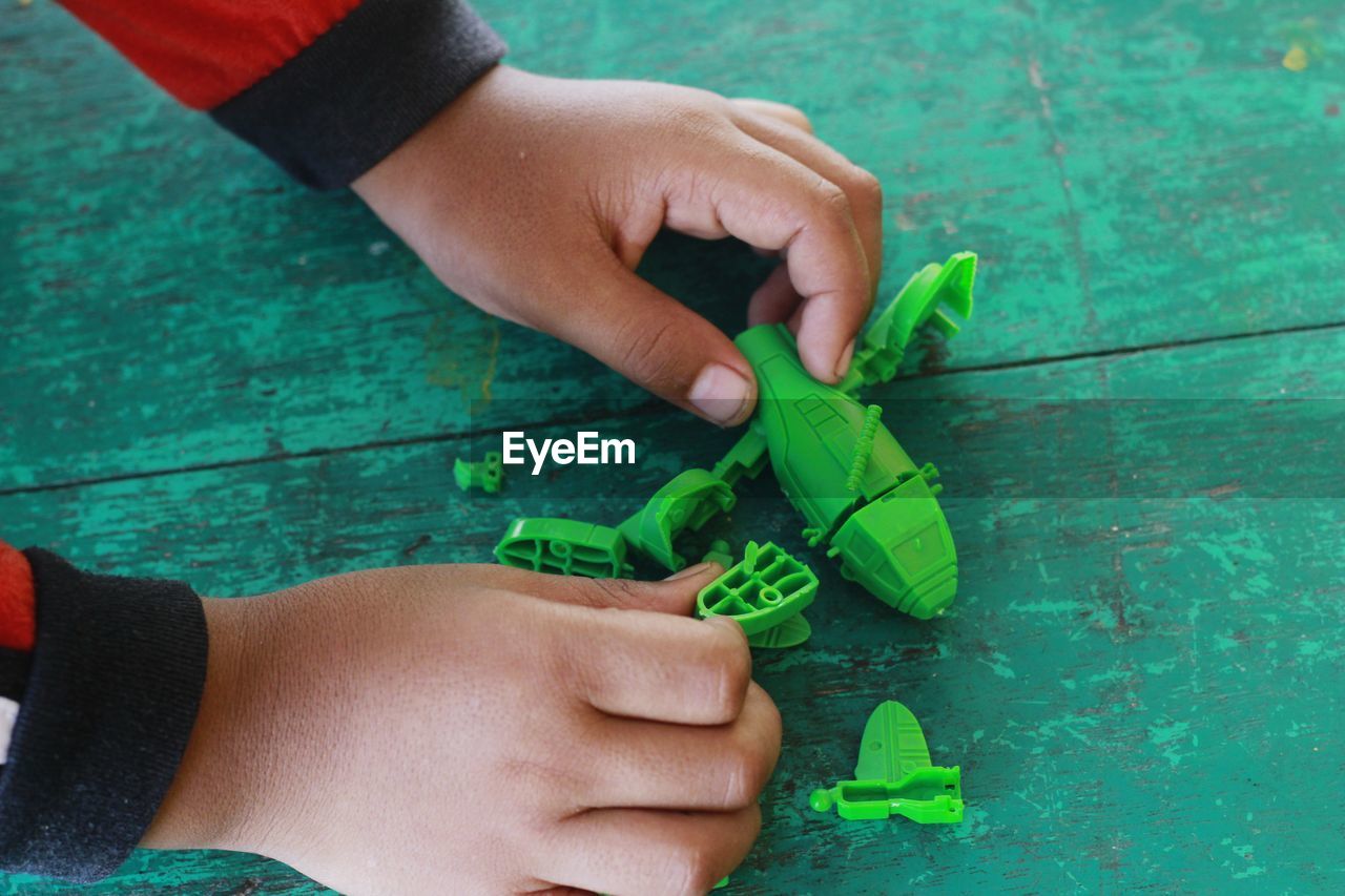 Cropped hands of child playing with green toy at table