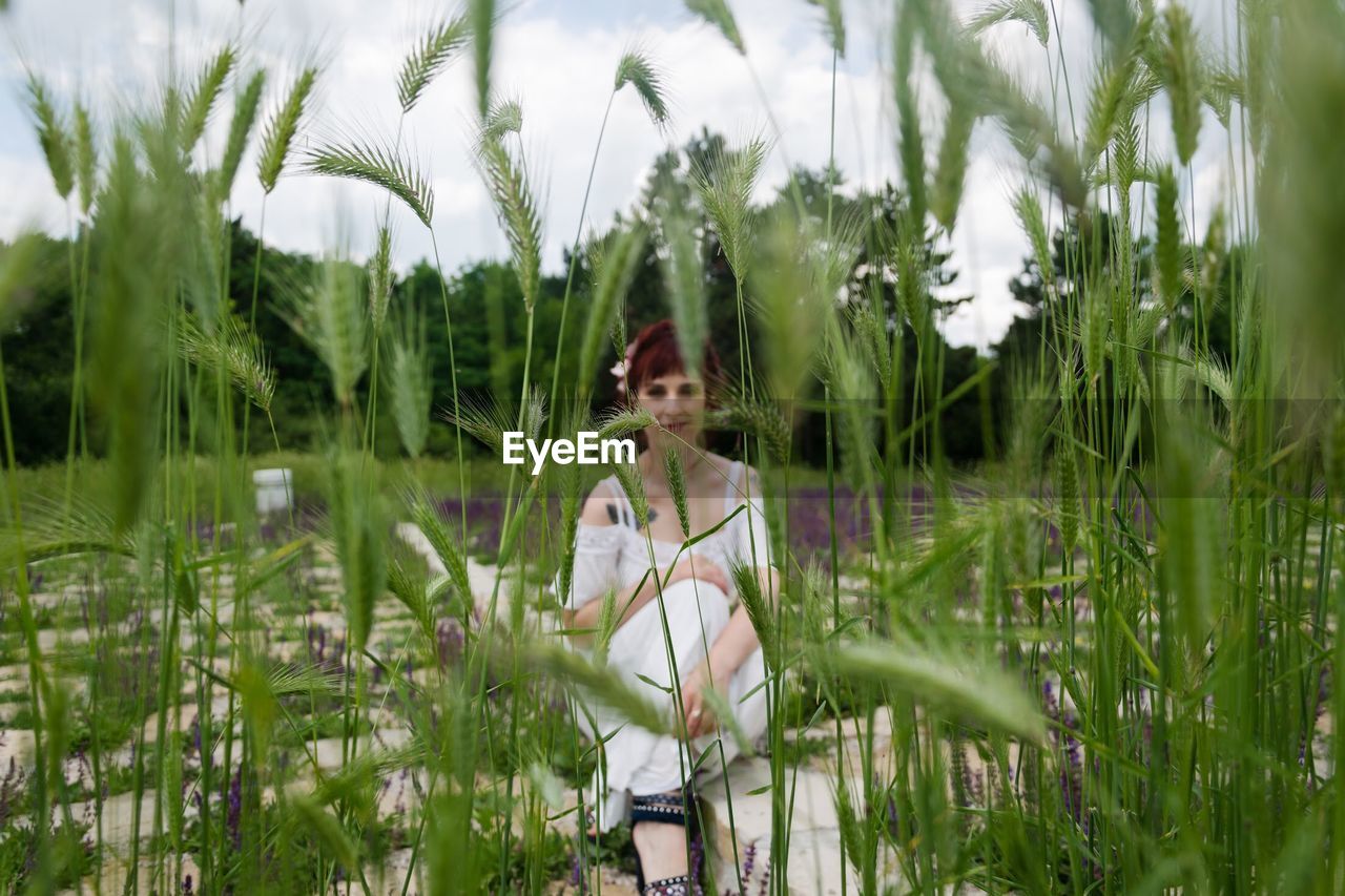 Portrait of young woman seen through plants on field