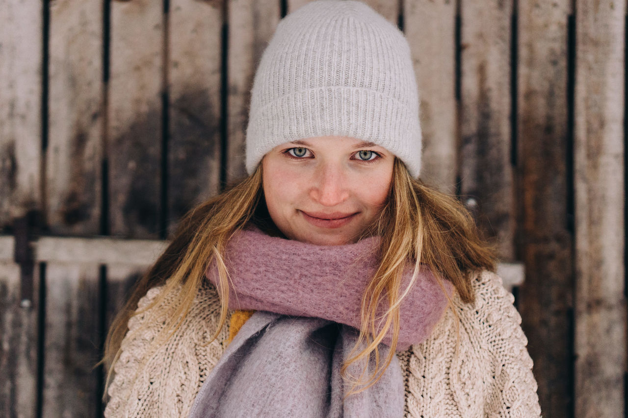 Portrait of woman wearing hat against log cabin  during winter