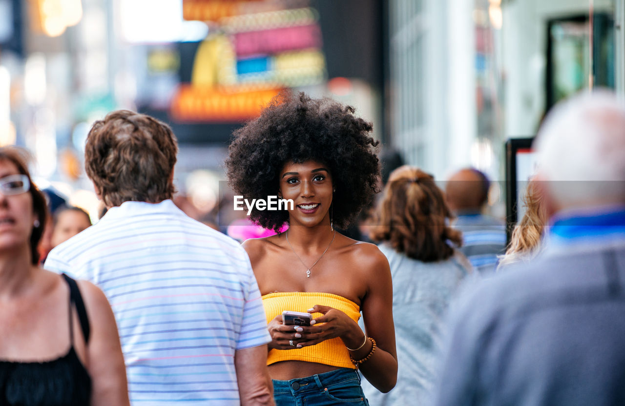 Portrait of happy young woman holding smart phone on city street