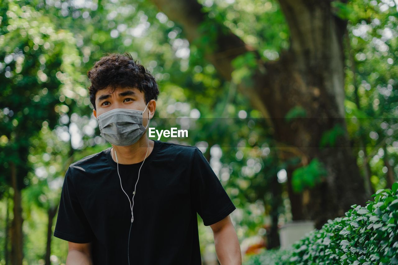 Young man wearing mask while standing against trees