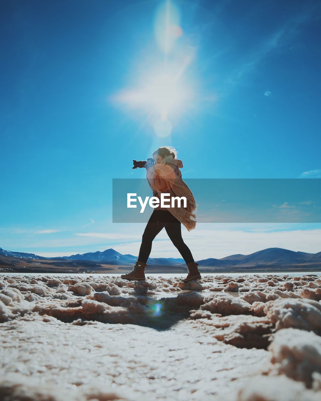 Side view of woman photographing while standing on landscape during sunny day