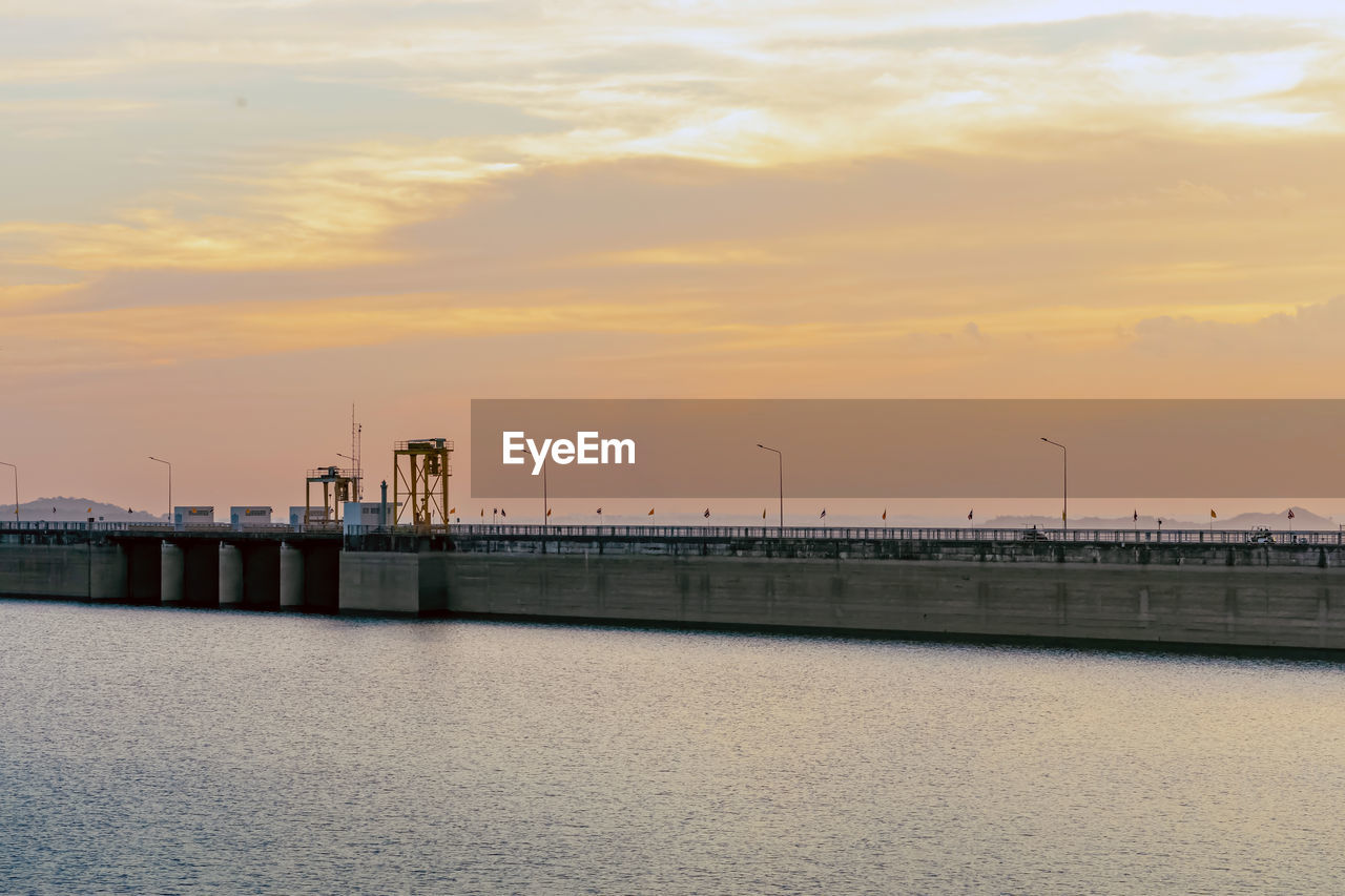 sky, pier, water, sunset, built structure, architecture, horizon, cloud, sea, nature, power generation, transportation, beauty in nature, ocean, industry, coast, dawn, waterfront, scenics - nature, outdoors, environment, bridge, tranquility, building exterior, no people, breakwater, tranquil scene, walkway, shore, technology, beach