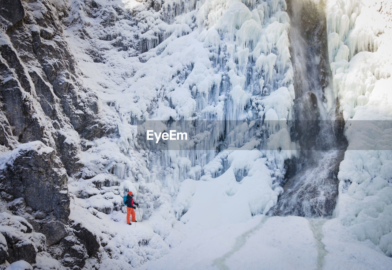 High angle view of man on snow covered mountains by waterfall during winter