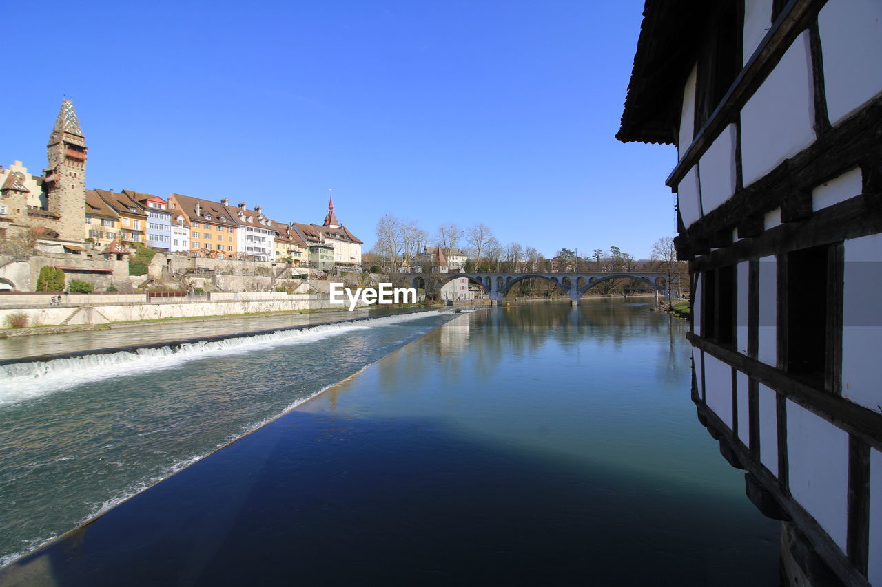 CANAL AMIDST BUILDINGS IN CITY AGAINST CLEAR BLUE SKY