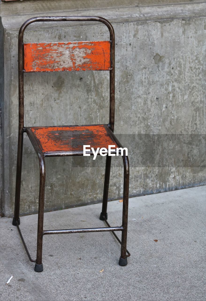 CLOSE-UP OF RUSTY CHAIR AGAINST ABANDONED WALL