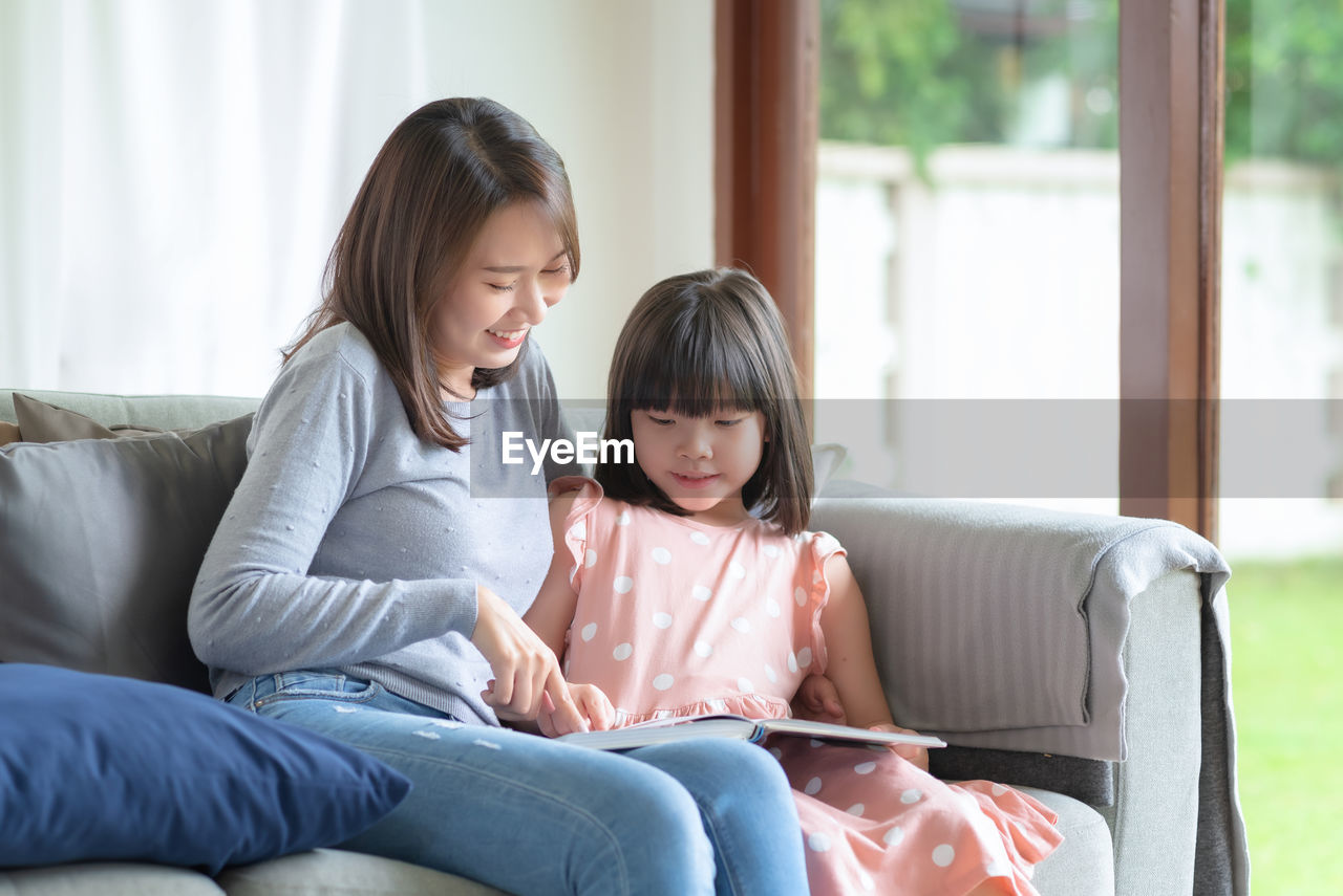 Happy asian mother teaching her cute kid daughter to studying in living room at home