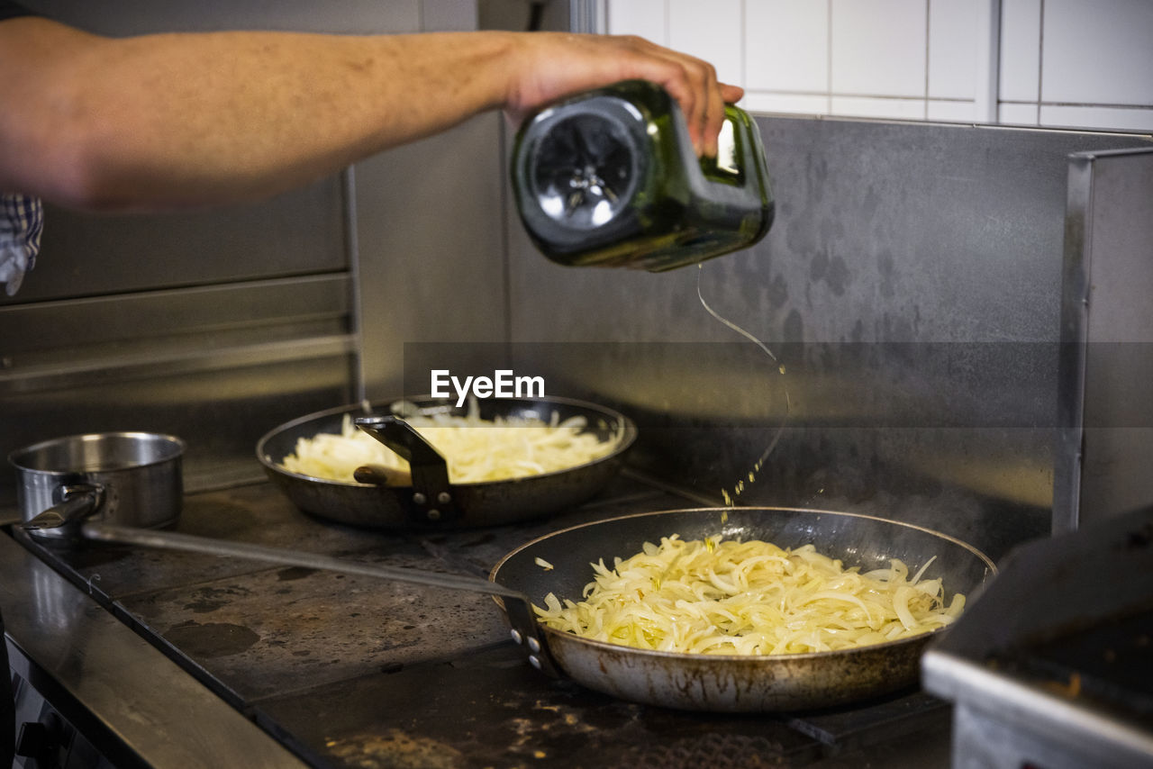 Cropped image of chef pouring oil on food in pan at restaurant kitchen