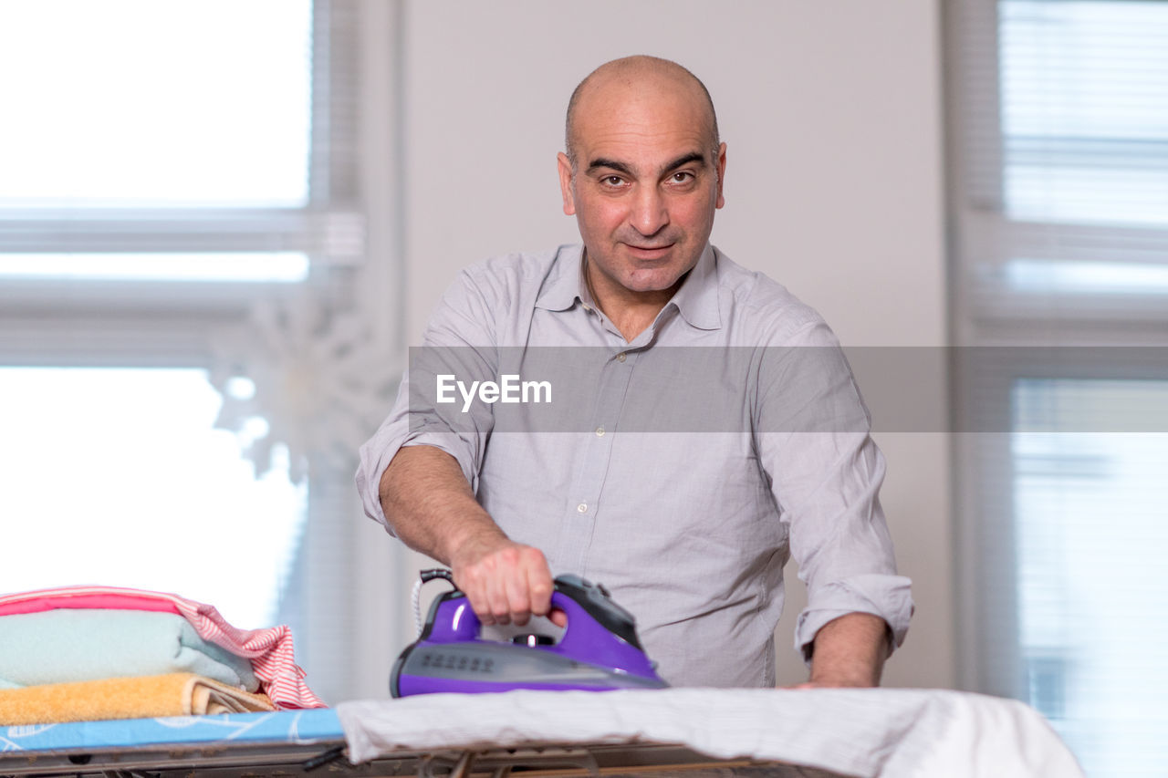 Portrait of man ironing clothes at home