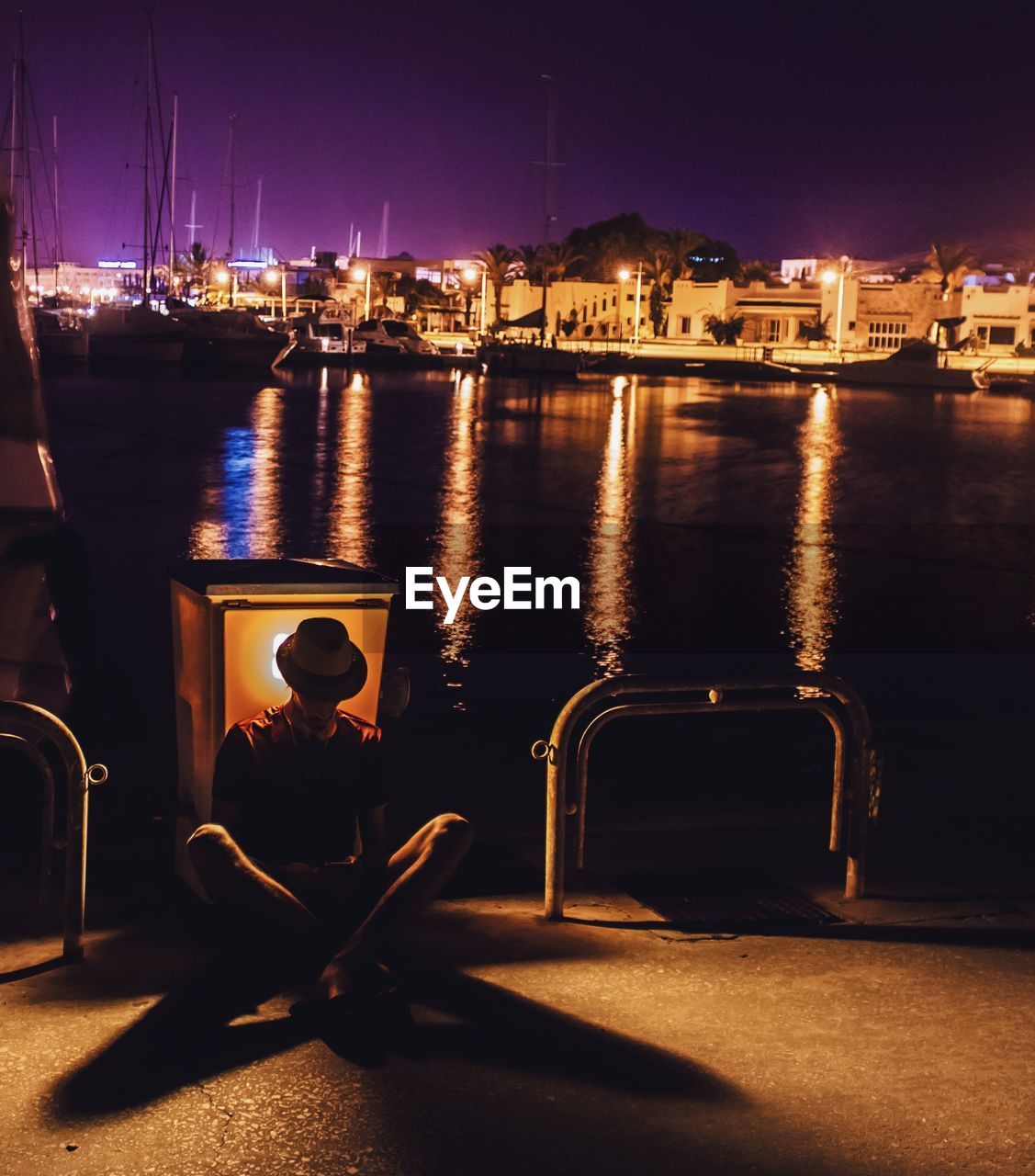 Man sitting at harbor in city during night