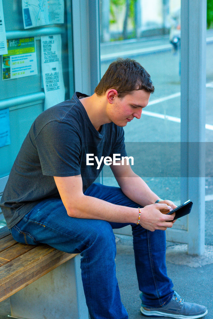 FULL LENGTH OF YOUNG MAN USING PHONE WHILE SITTING ON MOBILE