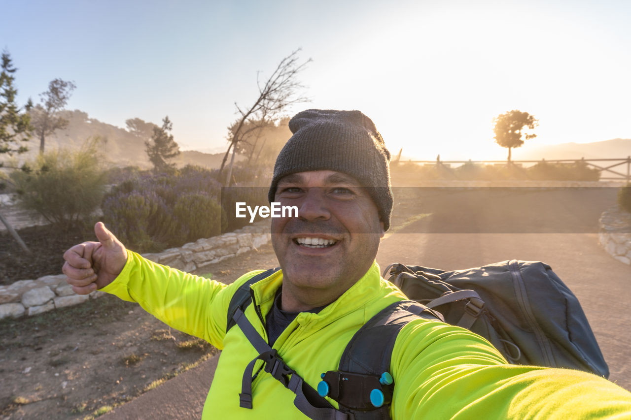 Male hiker takes a selfie with the sun rising from behind.