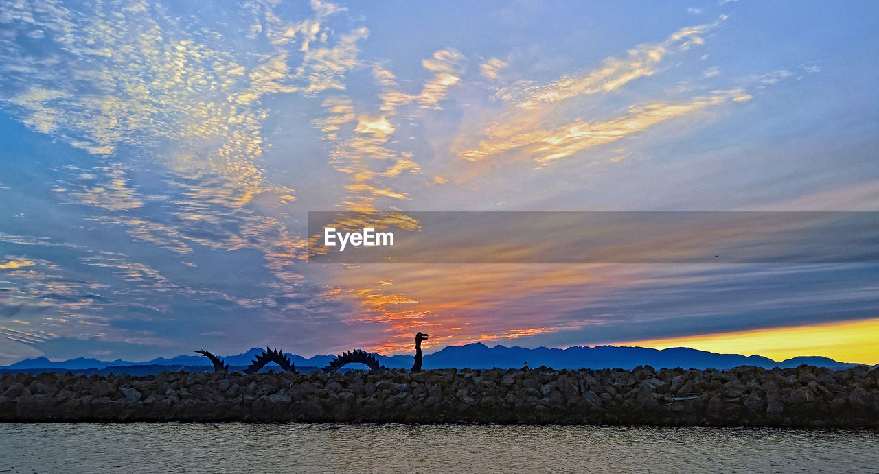 MAN STANDING IN SEA AGAINST SKY DURING SUNSET