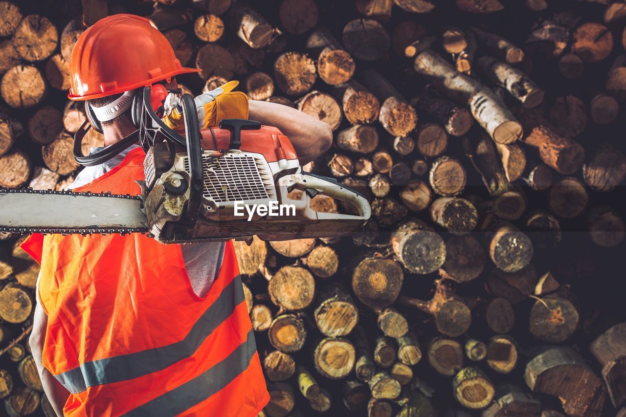 Rear view of worker holding machinery while standing by log