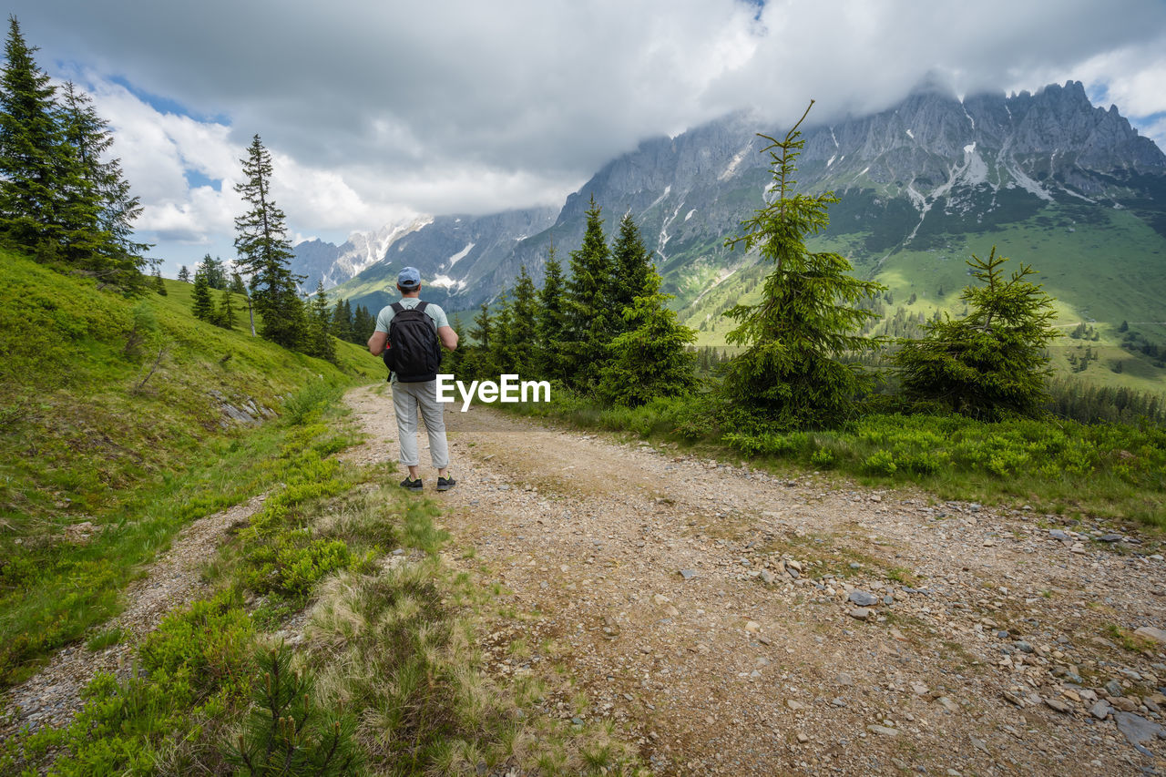 REAR VIEW OF MAN WALKING ON MOUNTAIN AGAINST SKY