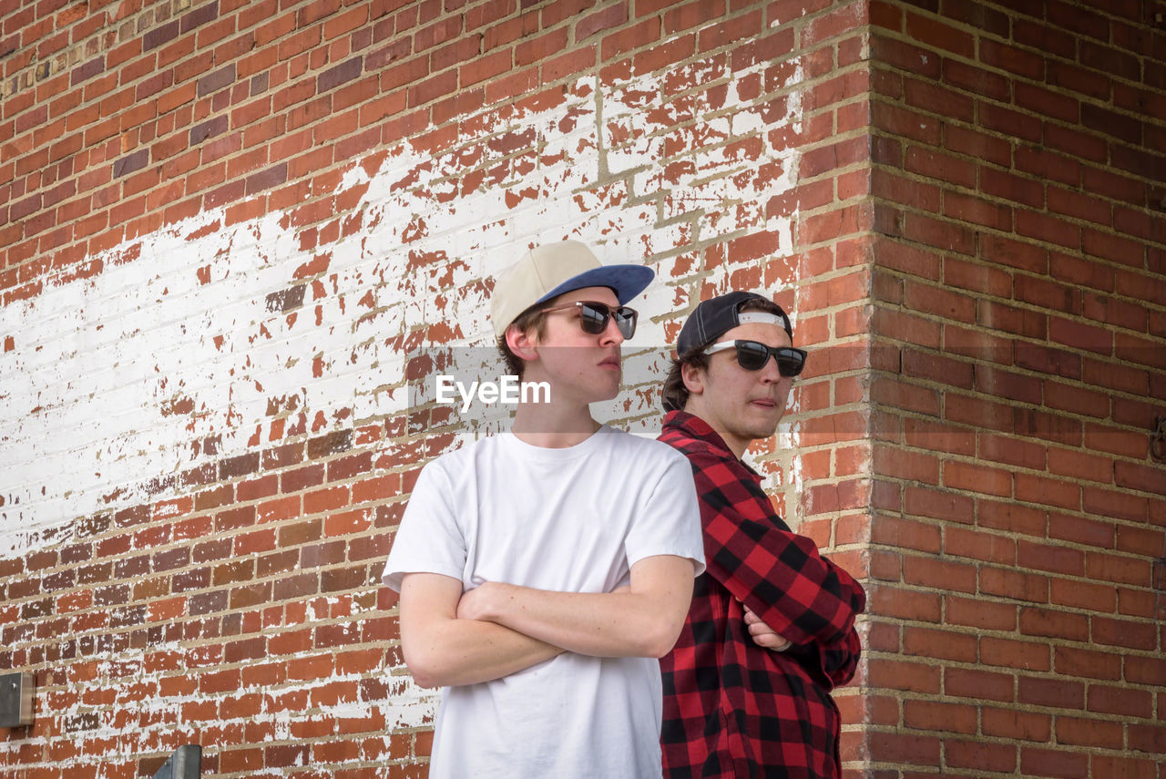 Confident young men wearing sunglasses against brick wall