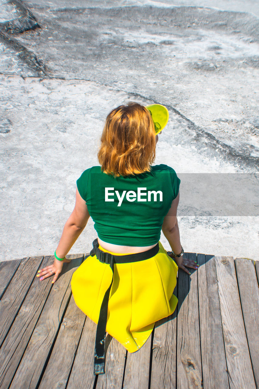 Rear view of woman sitting on boardwalk