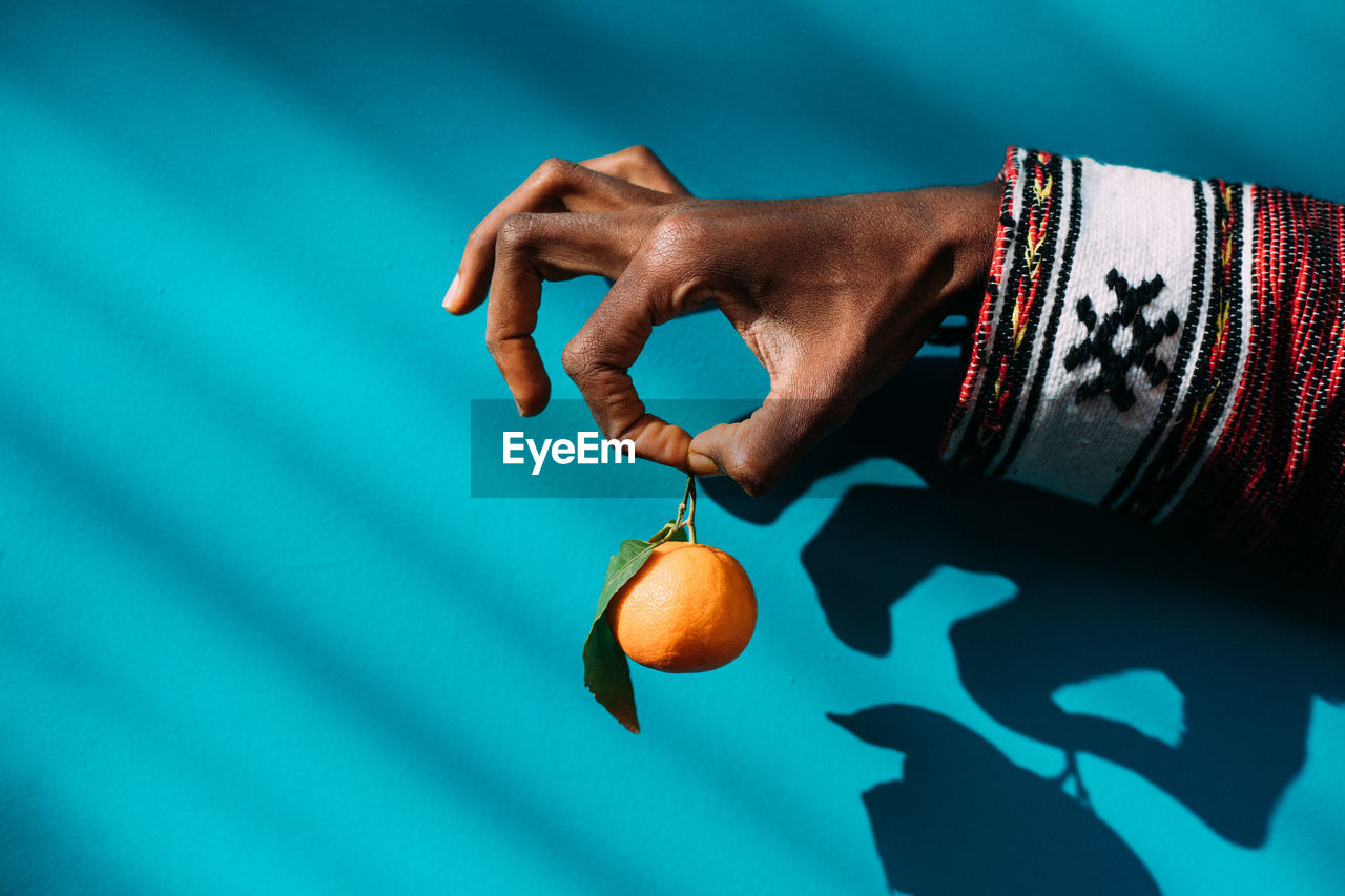 Cropped hand holding orange against wall