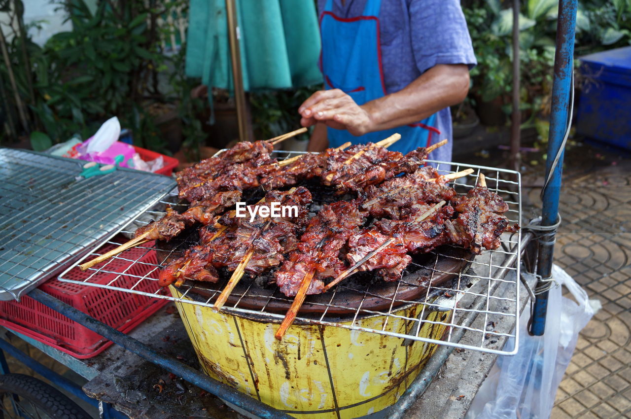 Midsection of man grilling meat on barbecue