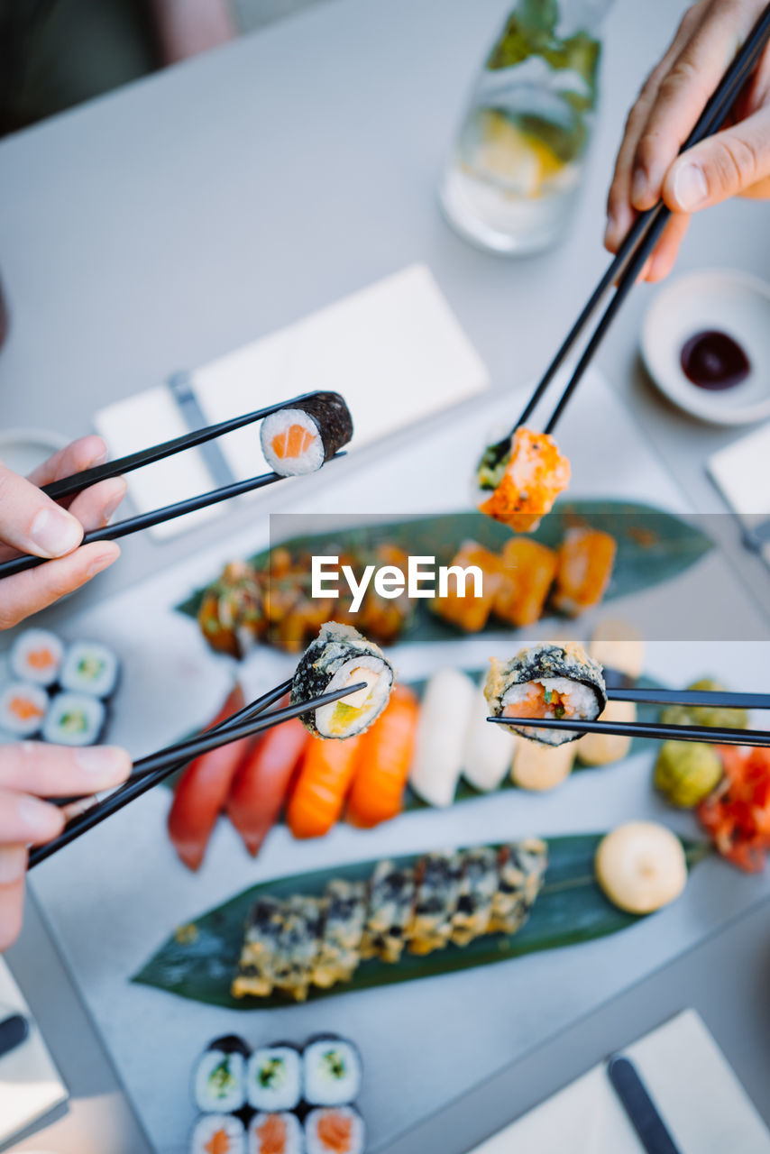 Vertical view of the friends hands holding sushi and rolls with wooden chopsticks