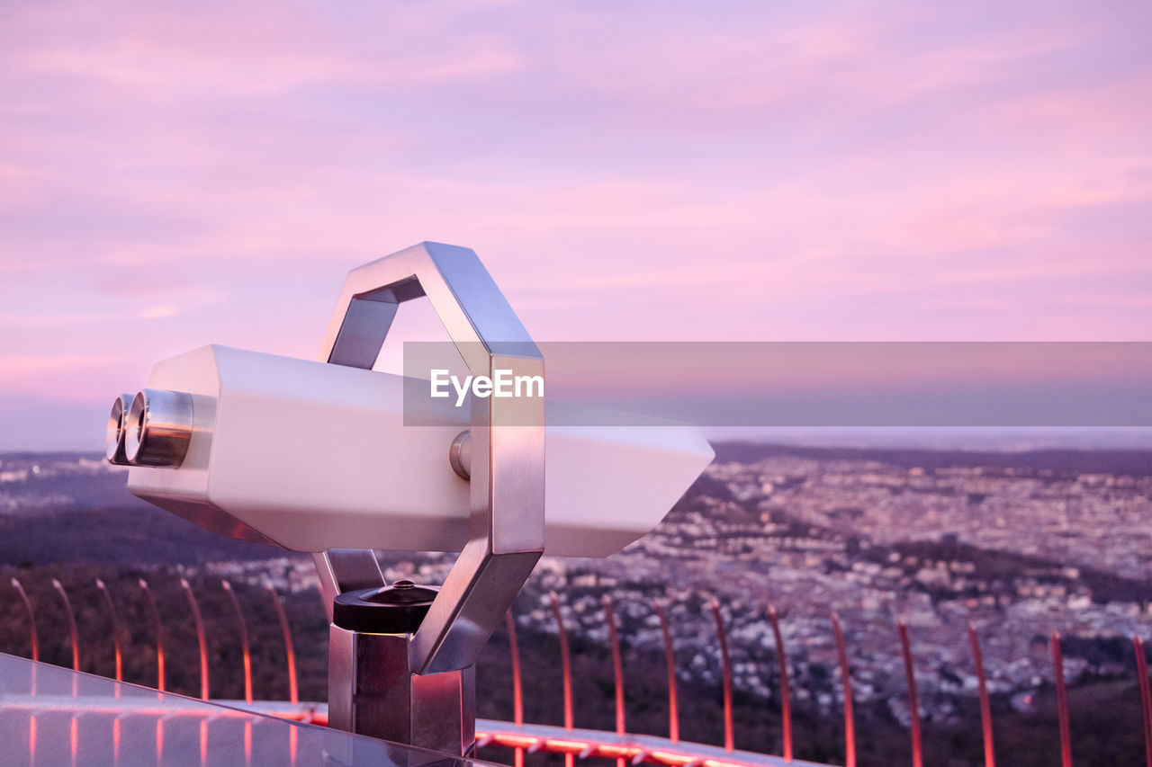 Coin operated binoculars overlooking cityscape against cloudy sky