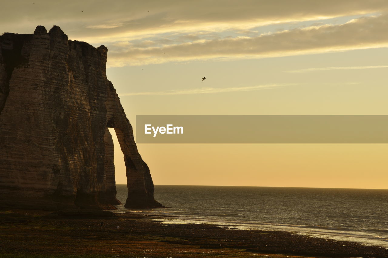 SCENIC VIEW OF ROCK FORMATION IN SEA AGAINST SKY DURING SUNSET