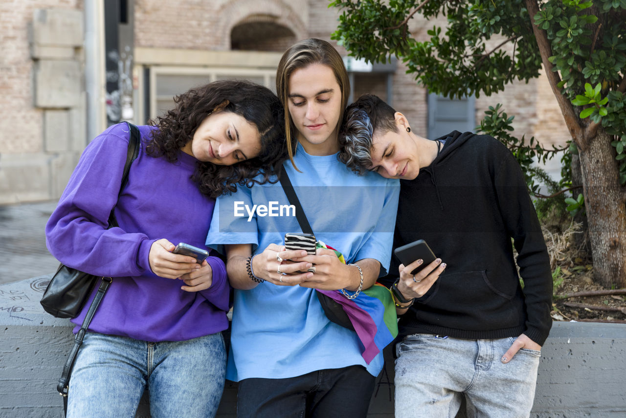 Friends using mobile phone while standing outdoors on the street.
