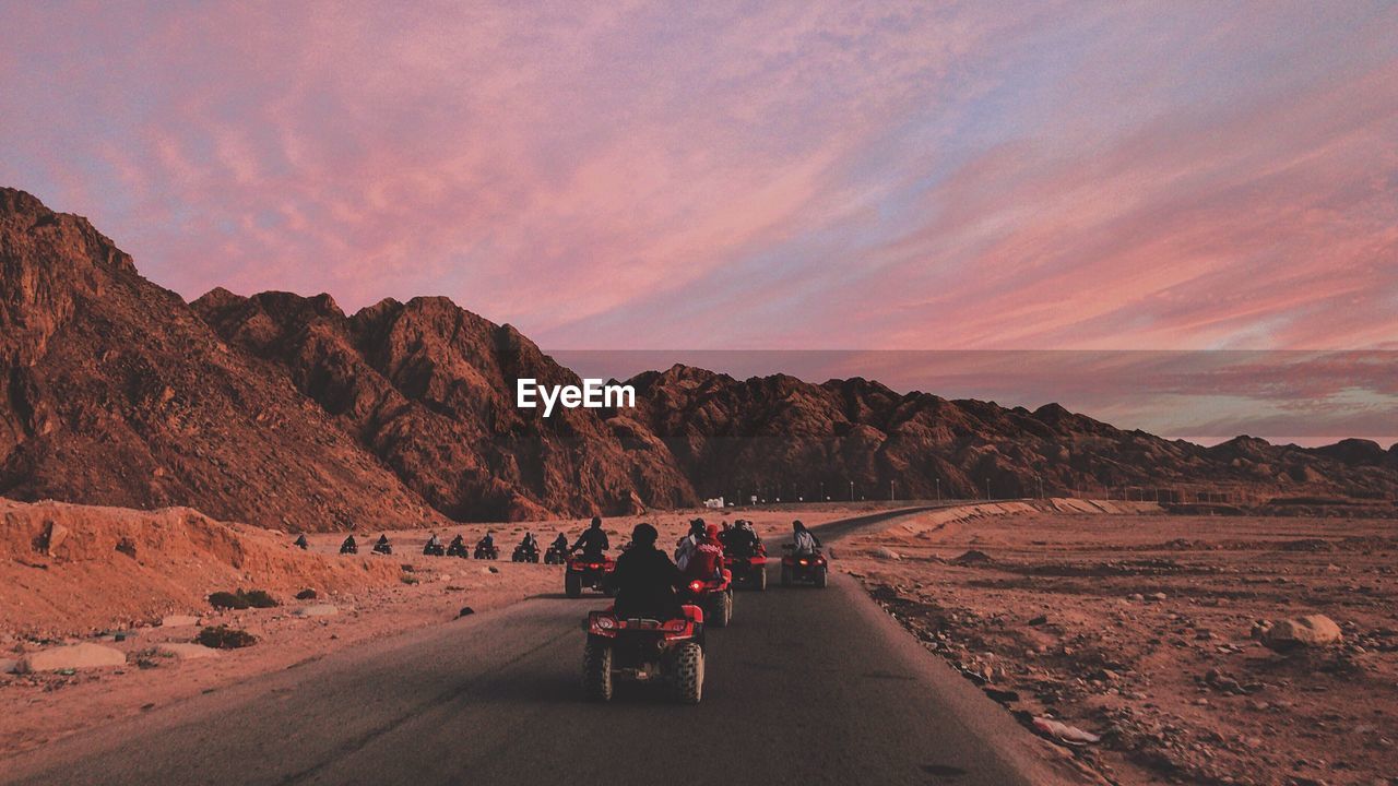 REAR VIEW OF PEOPLE RIDING BICYCLE ON ROAD AGAINST SKY