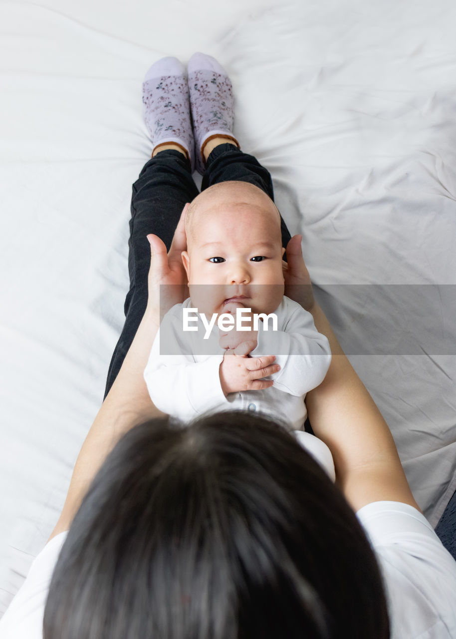 Young woman holding asian baby sitting on bed at home, asian mom and baby, smile, motherhood