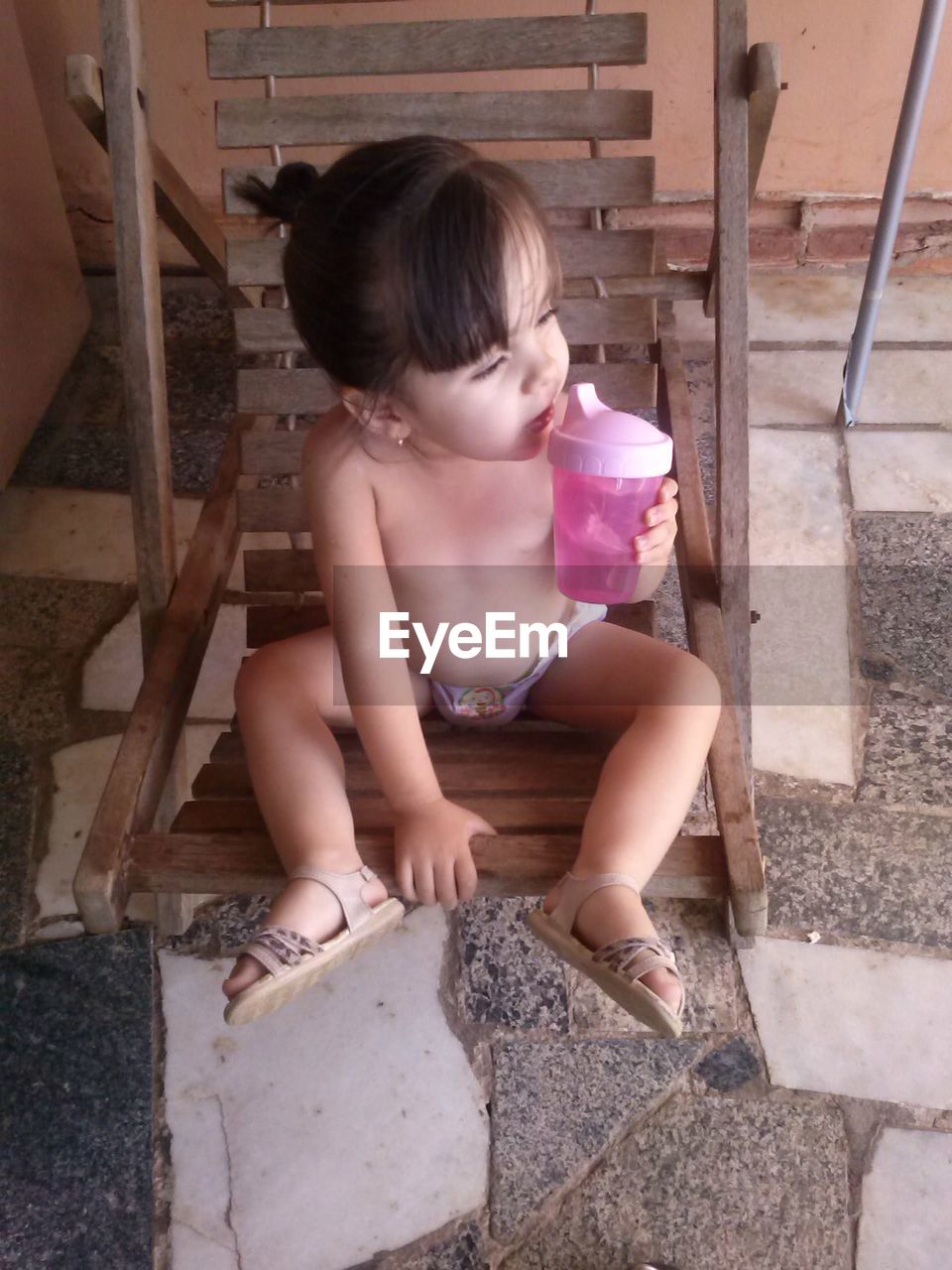 High angle view of shirtless girl drinking water while sitting on swing