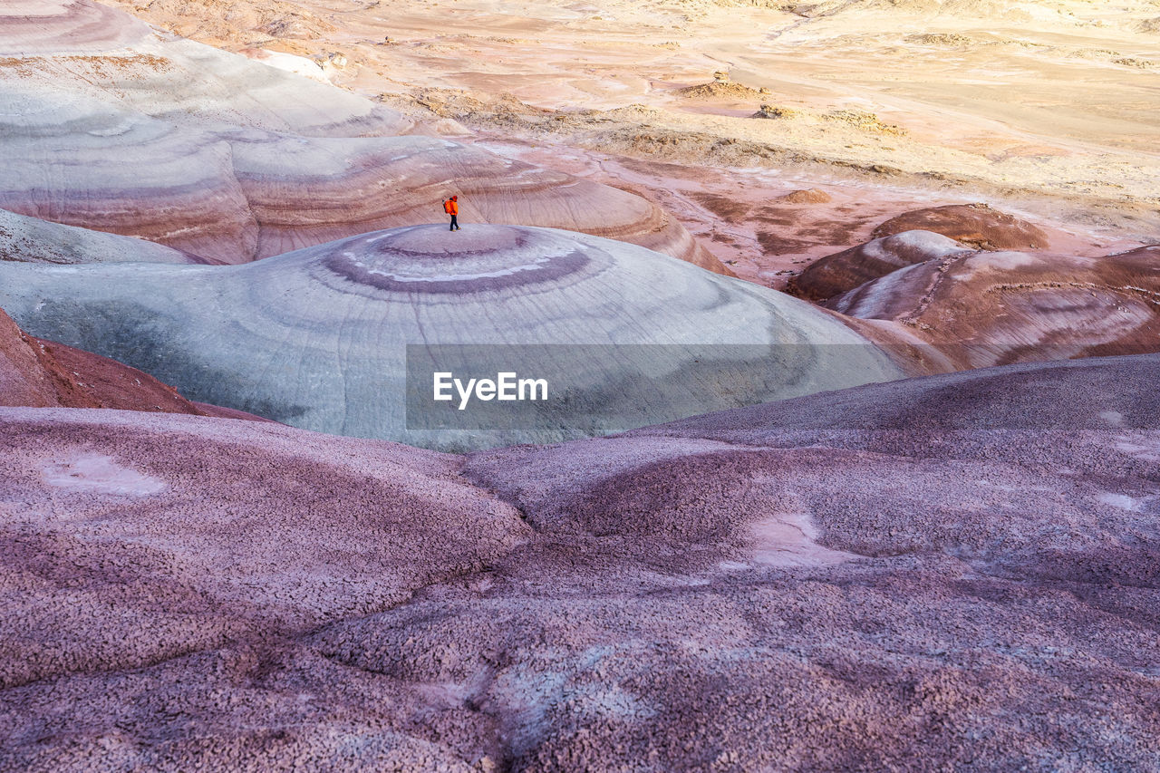 High angle of traveler in outerwear with backpack standing on top of smooth stone formation while exploring bentonite hills in utah, usa