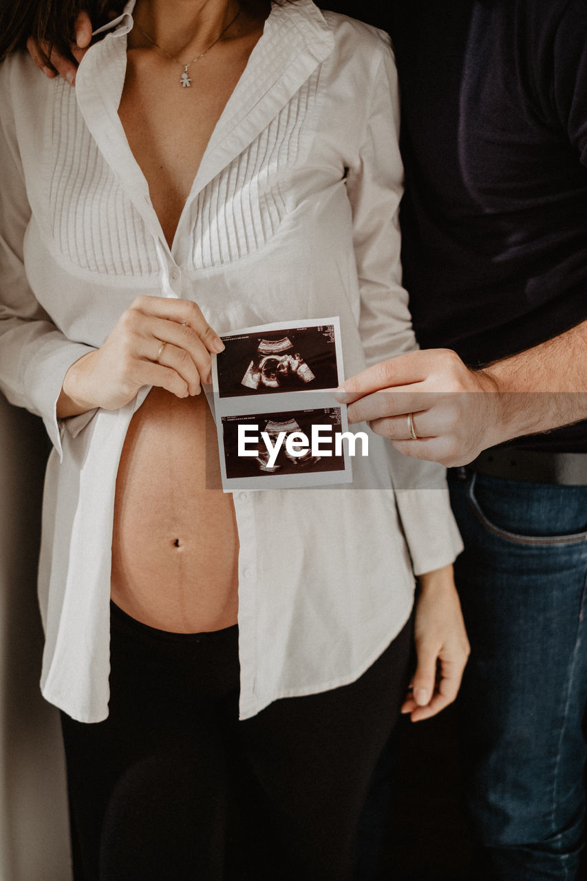 Midsection of couple holding ultrasound photograph of baby at home