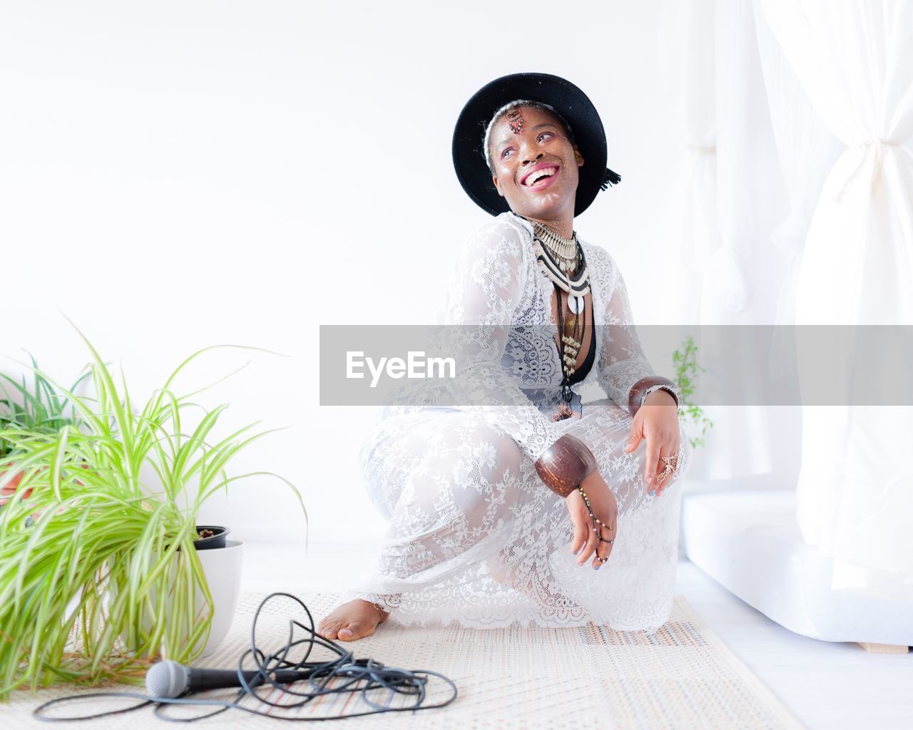 Smiling woman in dress looking away while crouching against white wall