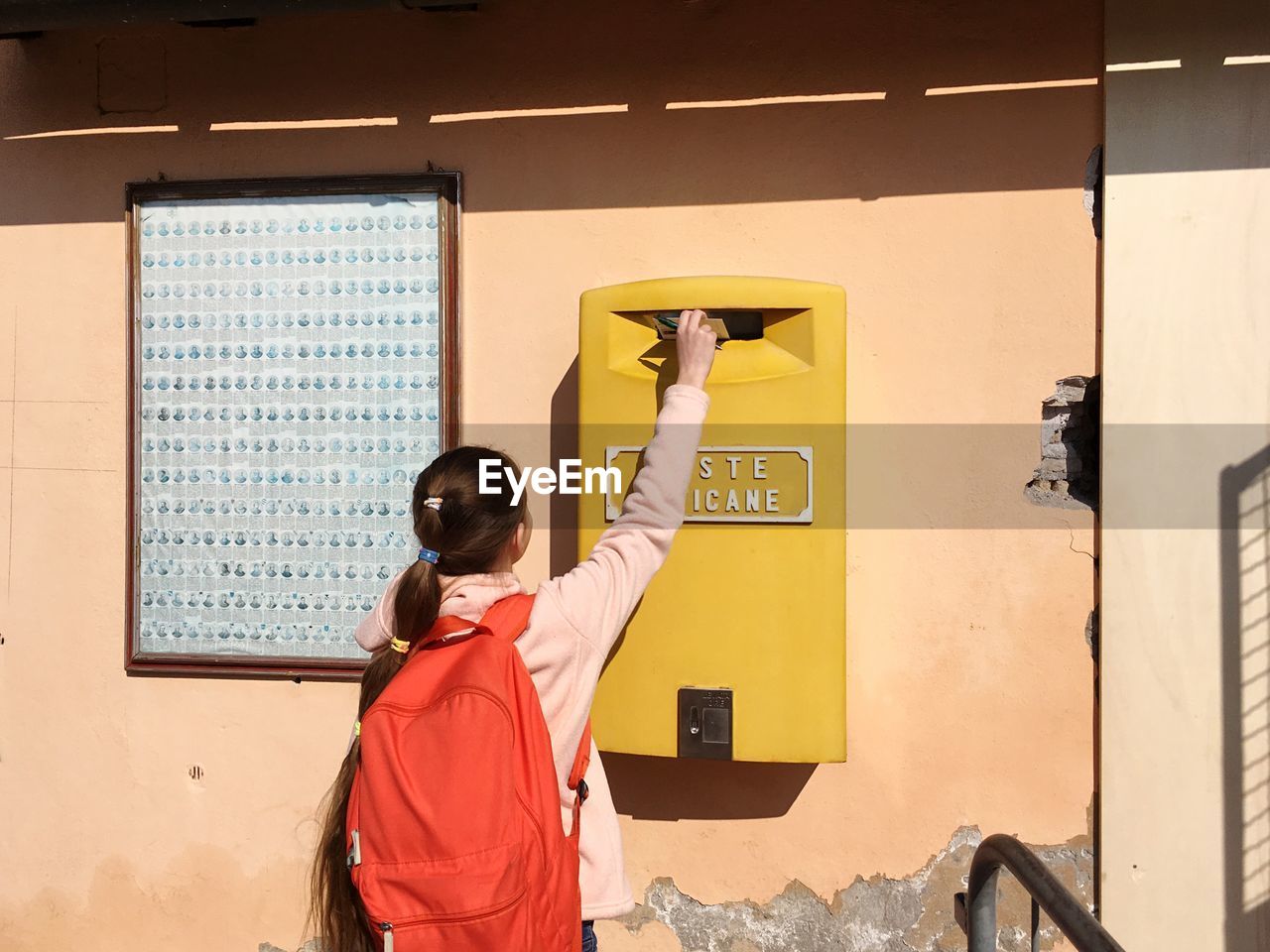 Rear view of girl putting letter in mailbox on wall 