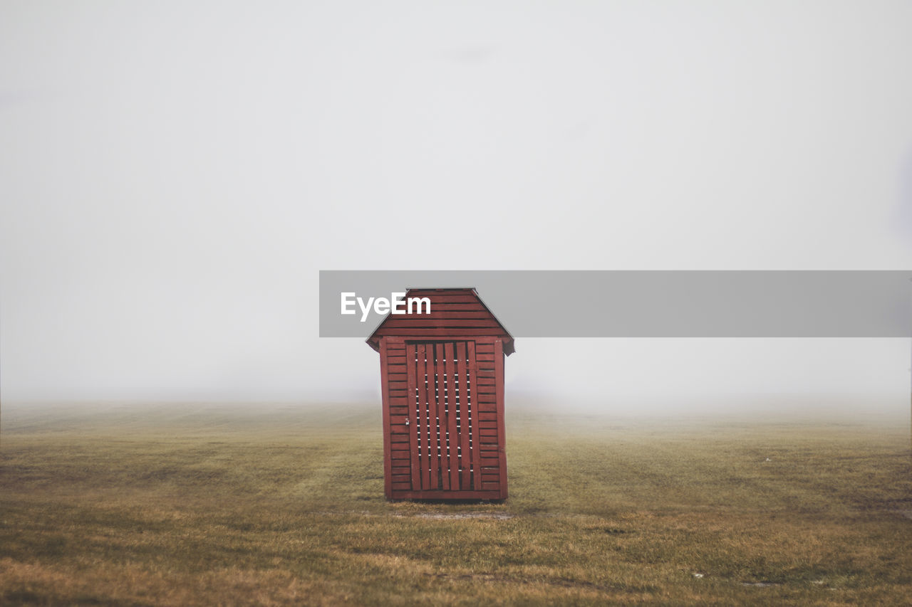 Wooden cabin on grassy filed against sky during foggy weather