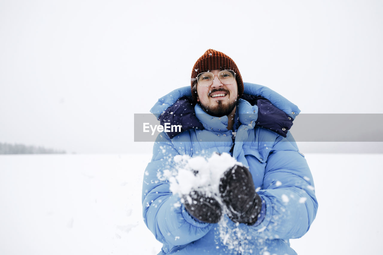 Smiling young man wearing padded jacket while playing on snow