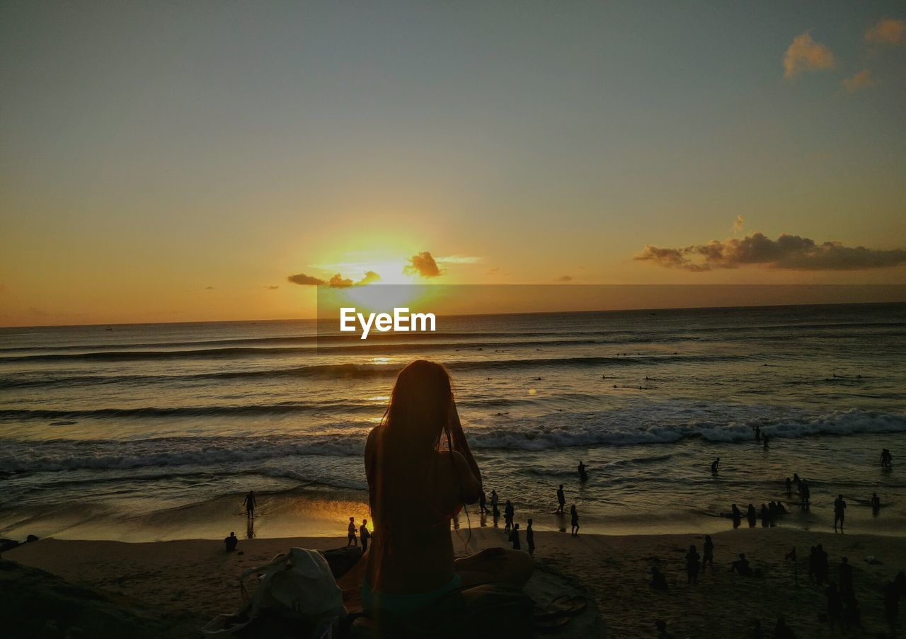 Woman sitting at beach against sky during sunset