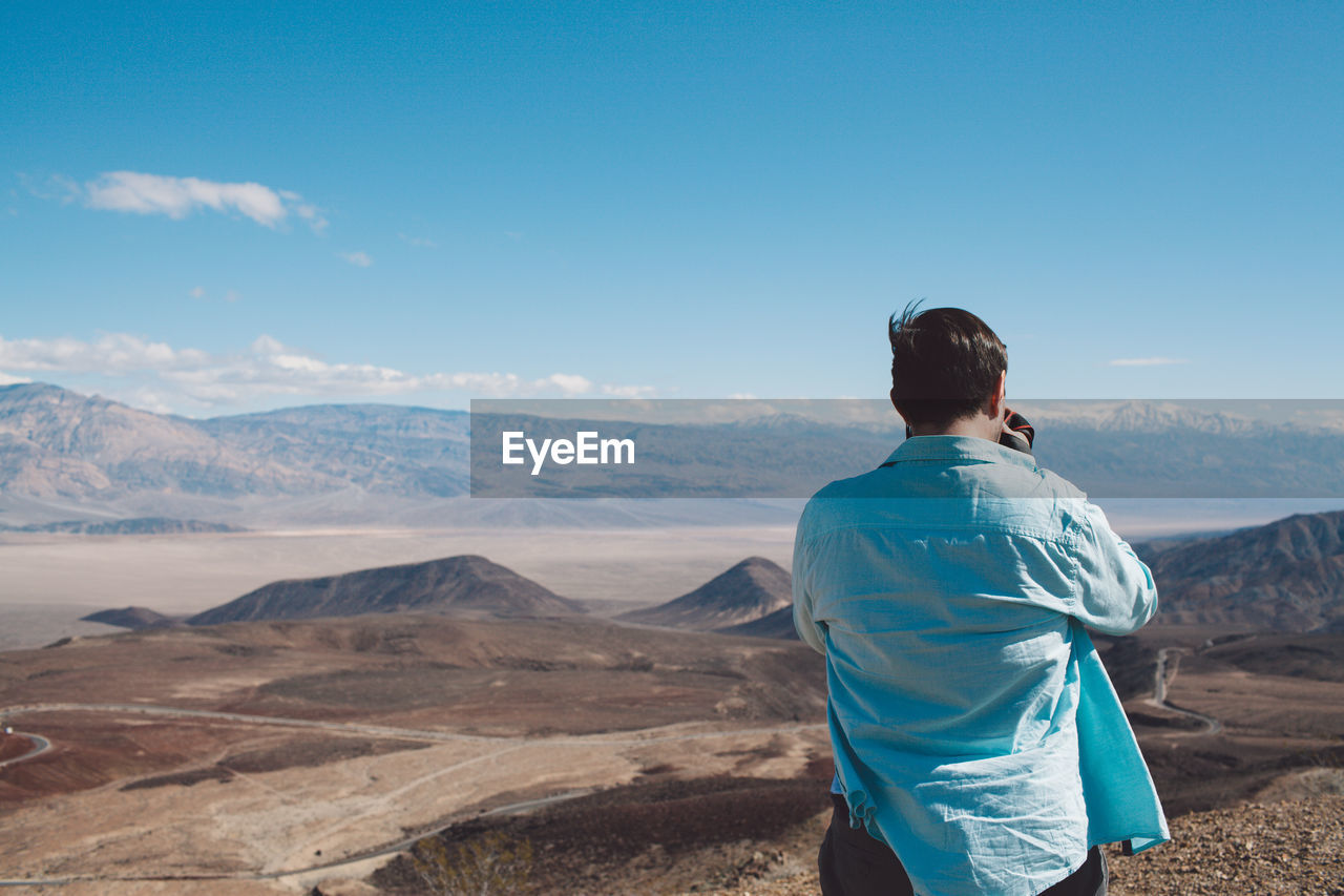 Rear view of man photographing landscape against sky