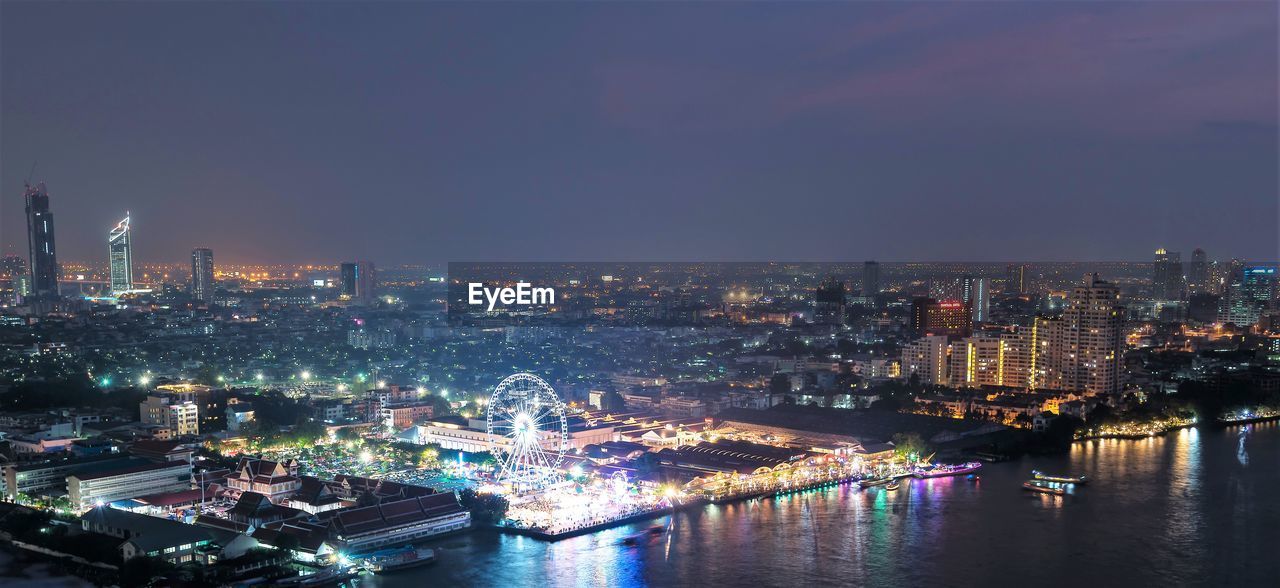 Illuminated city by river against sky at night