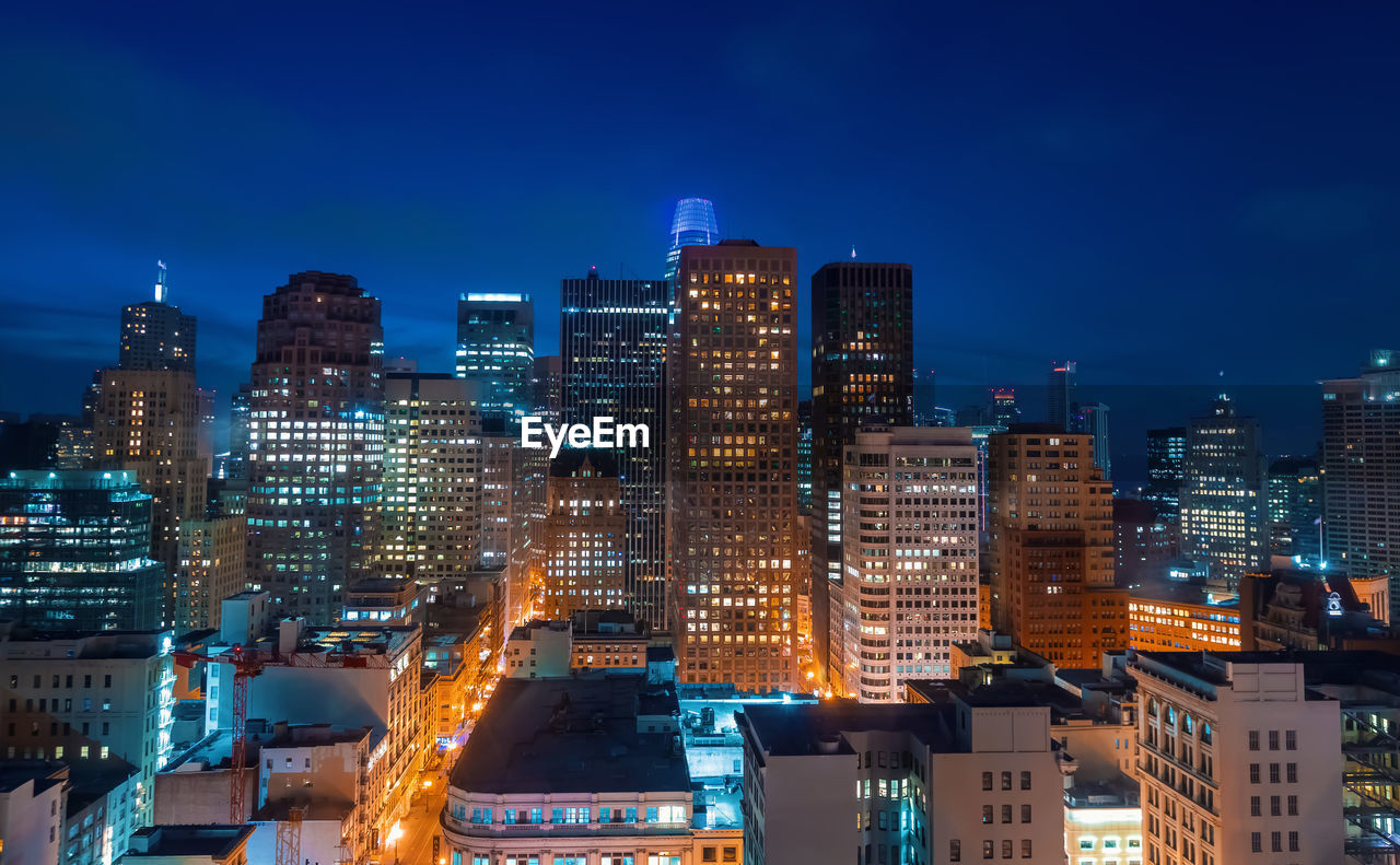 Illuminated buildings in city against sky at dusk