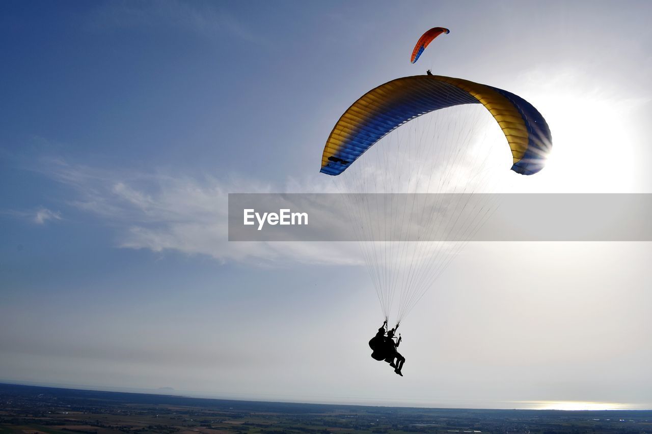 Person paragliding over landscape against sky