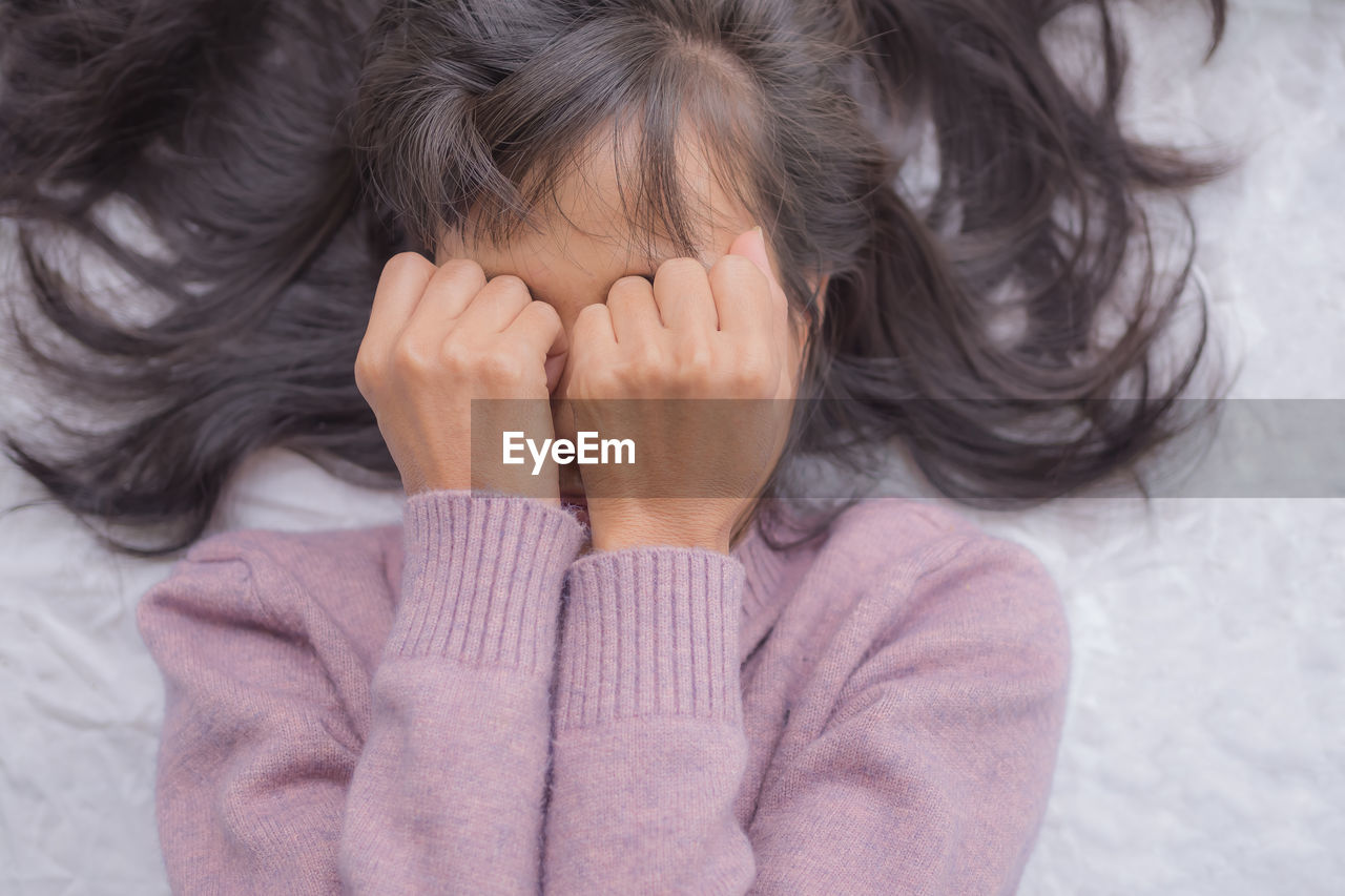 Close-up of girl covering face lying on bed