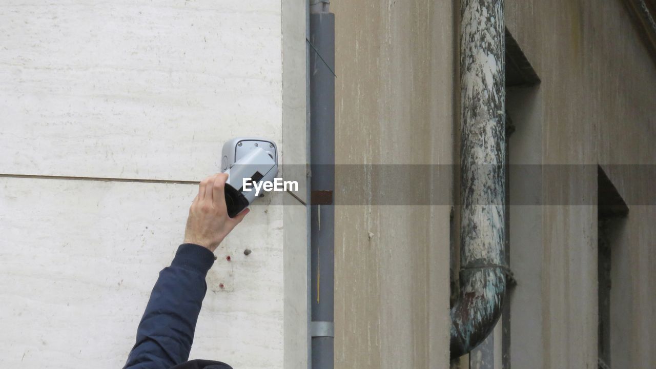 Cropped hand repairing security camera against wall