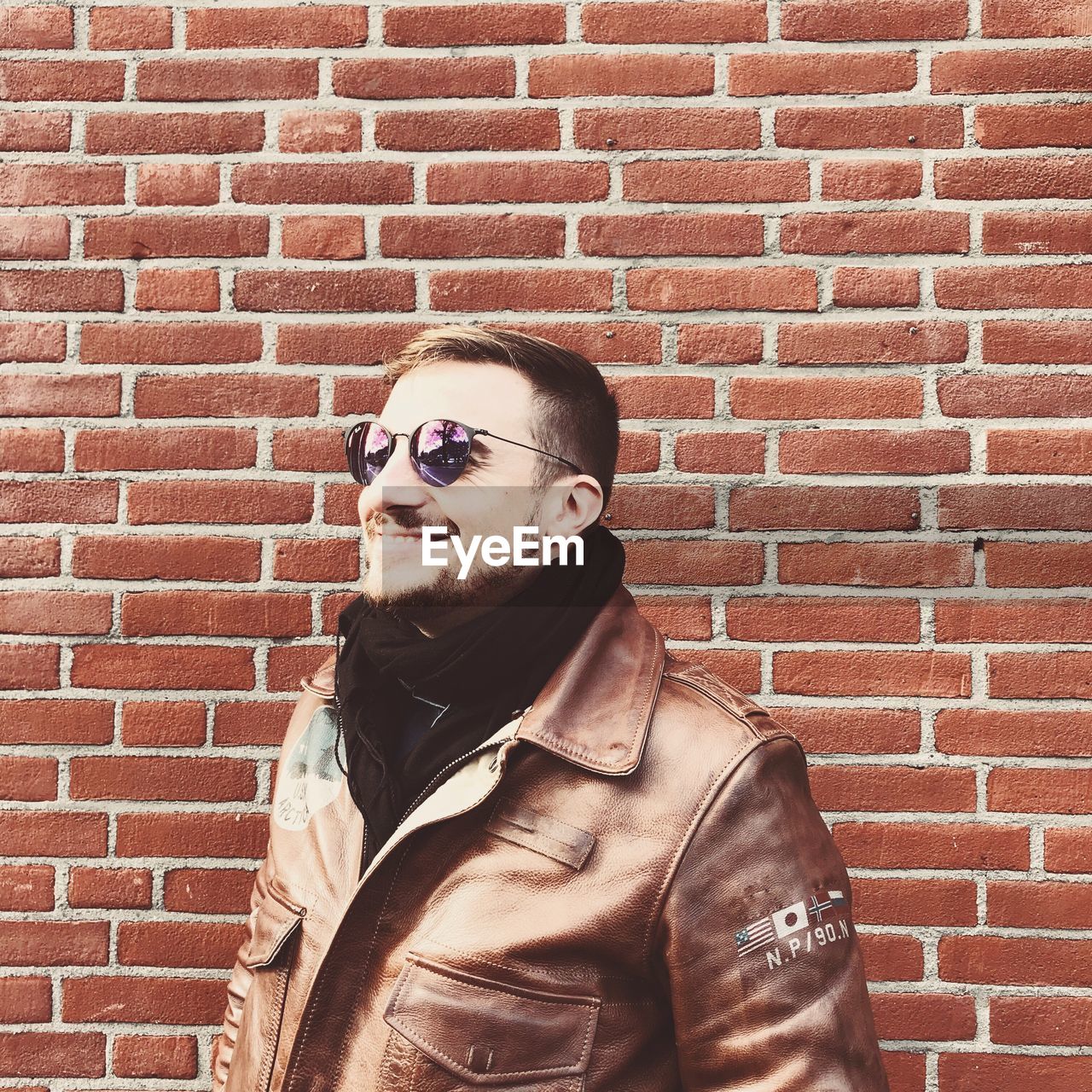 Smiling man wearing sunglasses against brick wall